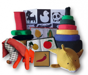A wide variety of play and learning materials are displayed, including fabric books with fruits and vegetables, stuffed animals like elephants and sharks, black-and-white high contract cards, and rings and blocks made of a stiff fabric.